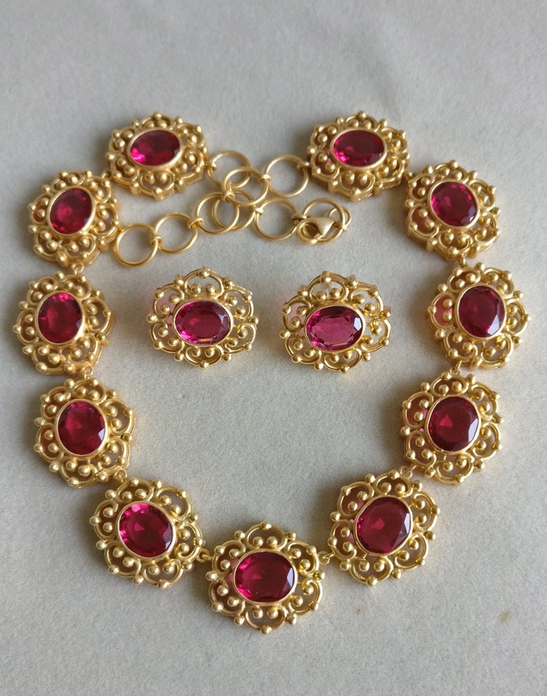 May include: A gold necklace with a delicate filigree design and oval-shaped red gemstones. Matching earrings with the same design and gemstones are included.
