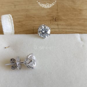 May include: A pair of silver stud earrings with clear round cubic zirconia stones. The earrings are on a white background.