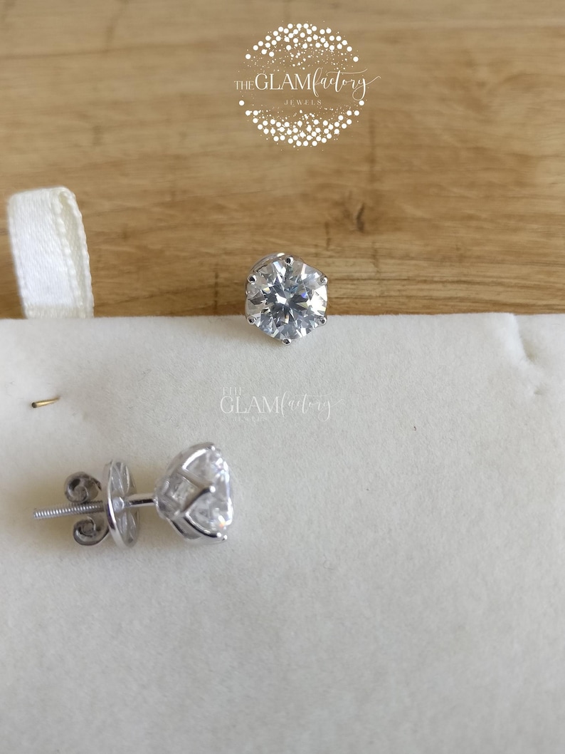 May include: A pair of silver stud earrings with clear round cubic zirconia stones. The earrings are on a white background.