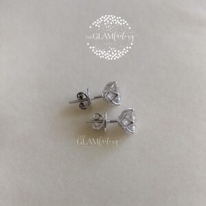 May include: A pair of silver stud earrings with a clear, round gemstone in a prong setting. The earrings are on a white surface.