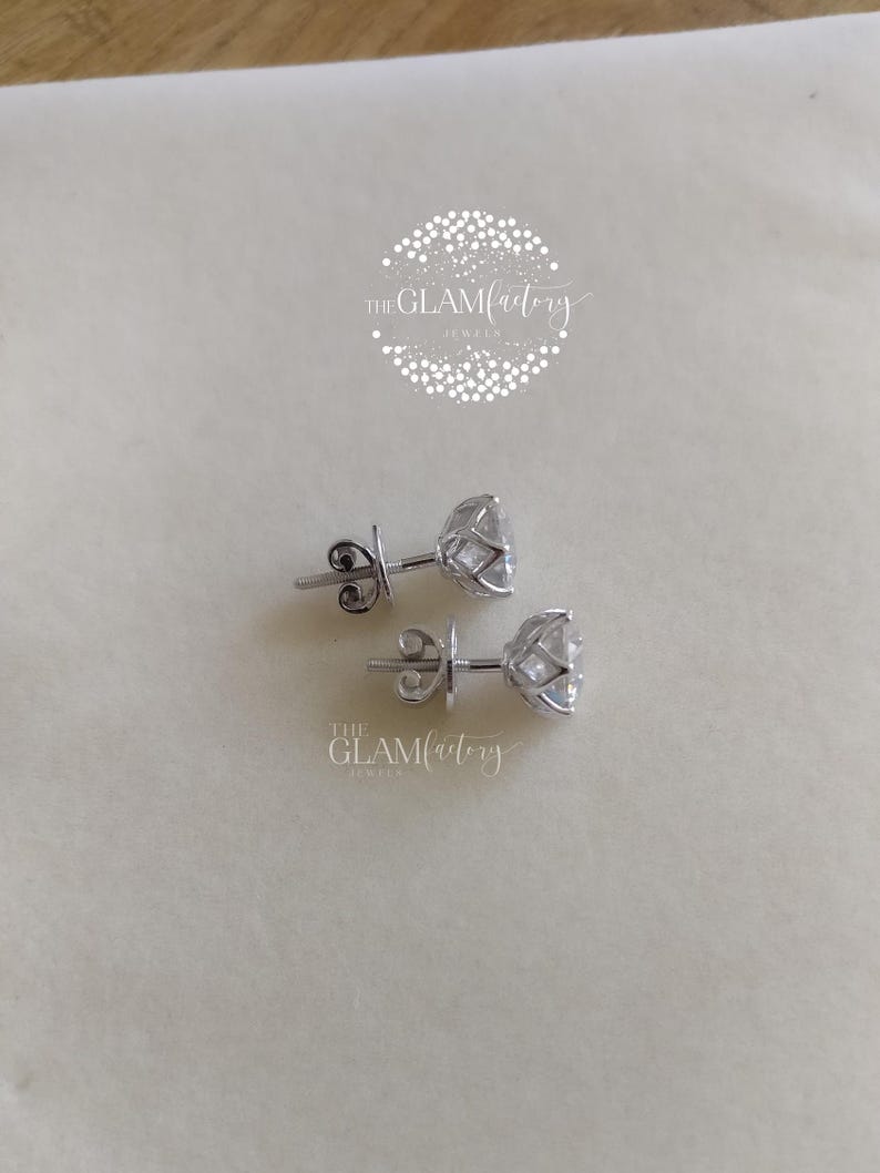 May include: A pair of silver stud earrings with a clear, round gemstone in a prong setting. The earrings are on a white surface.