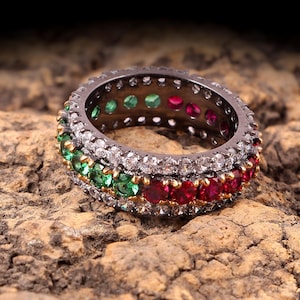 以下が含まれることがあります： 3列の宝石がついた黒い指輪。上の列は白、真ん中の列は緑、下の列は赤です。