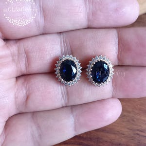 Puede incluir: Un par de pendientes de oro con una gran piedra preciosa azul de forma ovalada rodeada de peque&ntilde;as piedras preciosas blancas.