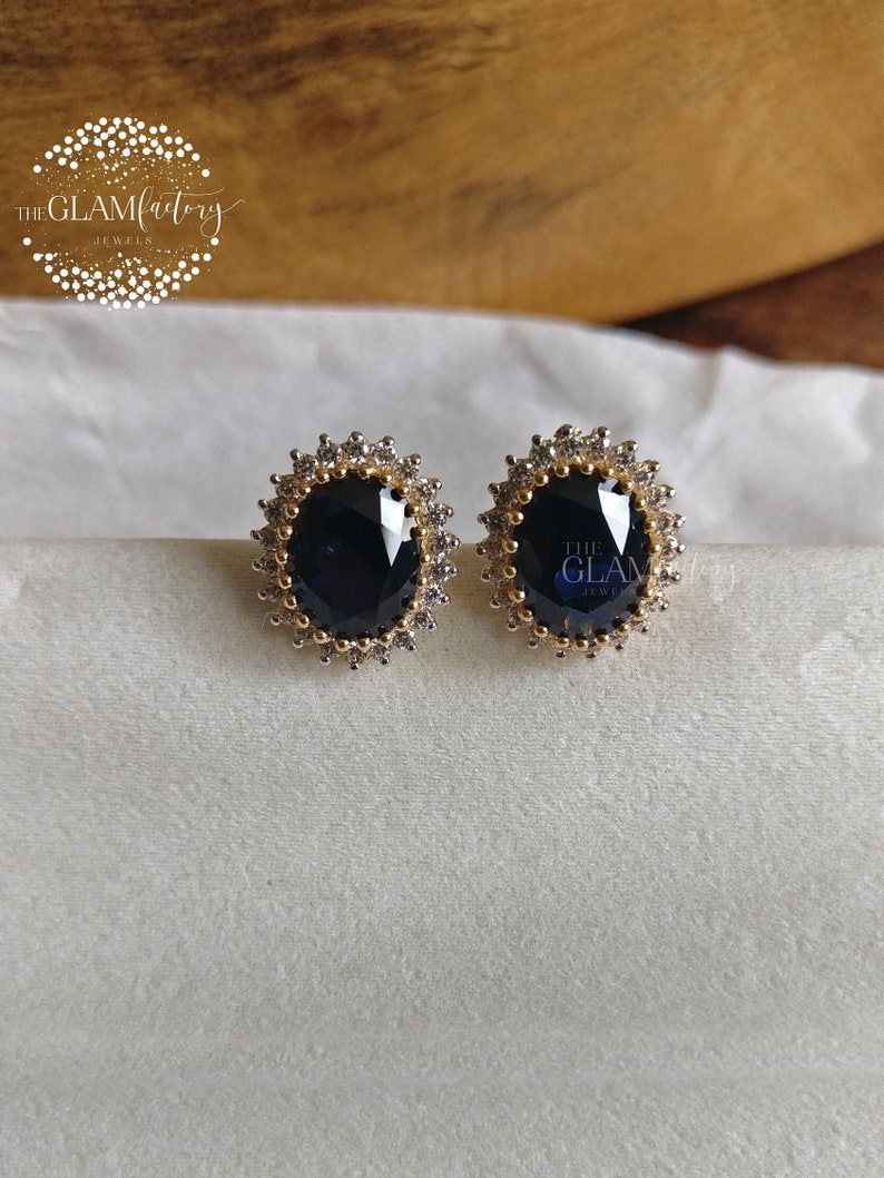 Puede incluir: Un par de pendientes de oro con una piedra ovalada azul oscuro rodeada por un halo de piedras transparentes m&aacute;s peque&ntilde;as.
