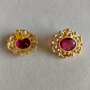 May include: A pair of gold earrings with ornate filigree designs and oval-shaped red gemstones.