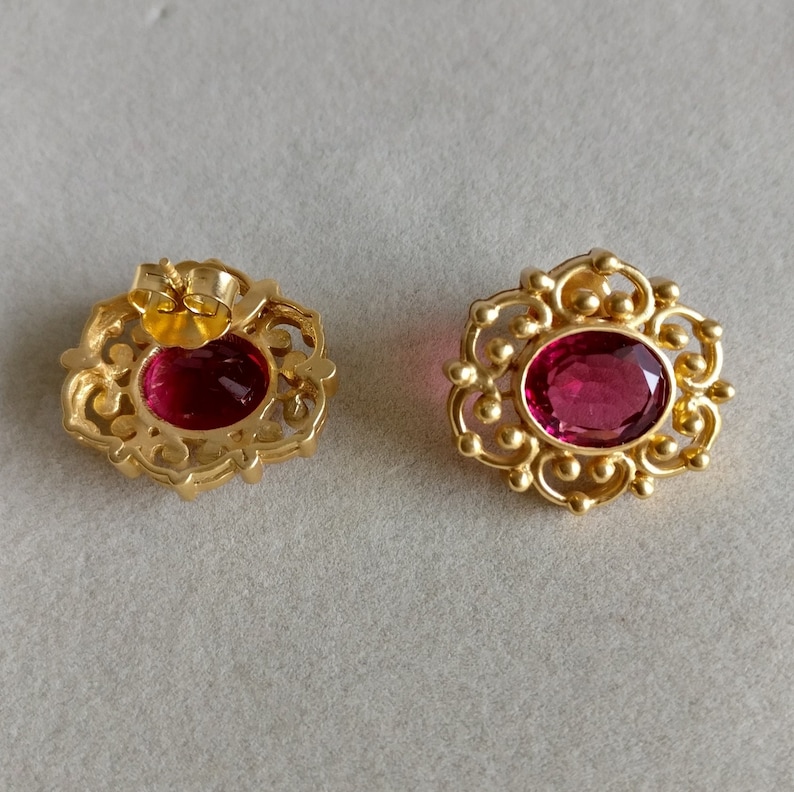 May include: A pair of gold earrings with ornate filigree designs and oval-shaped red gemstones.