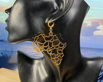 May include: Gold-colored earrings in the shape of the African continent, with detailed outlines of countries. The earrings are suspended from gold-colored lever-back closures. The earrings are displayed on a black mannequin head.