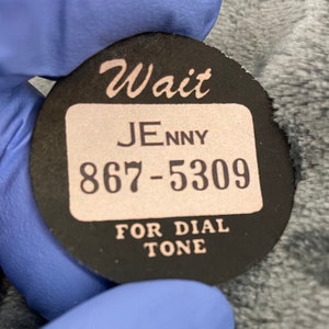 May include: A black round sticker with white text that reads "Wait for dial tone" and a pink label with the text "Jenny 867-5309".