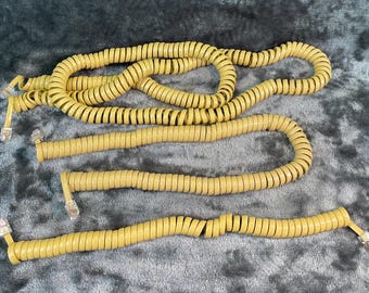 May include: Three beige coiled telephone cords with clear plastic modular connectors at each end. The cords are arranged in a horizontal layout, with one long cord looped in a circle and two shorter cords positioned straight below it.