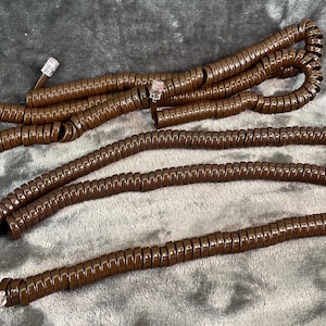 Puede incluir: Un cable de teléfono en espiral de color marrón con dos conectores RJ-11.