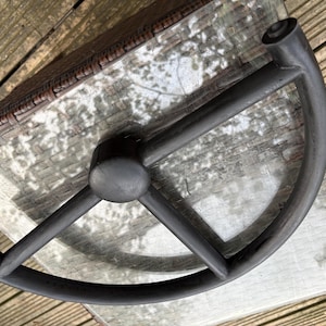 Puede incluir: Un objeto de metal gris oscuro con un diseño circular, con un cubo central y brazos curvos. El objeto está colocado sobre una superficie de vidrio, con una superficie marrón tejida en el fondo.