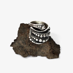 Op de afbeelding: Een zilveren ring met een getextureerd, organisch ontwerp. De ring is gemaakt van meerdere banden die om de vinger wikkelen. De banden zijn versierd met kleine, ronde kralen.
