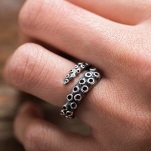 May include: A silver octopus ring with a detailed design. The ring is wrapped around a finger.