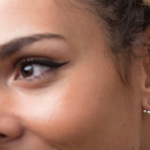 May include: A close-up of a person's ear with a silver ear cuff featuring multiple small round beads. The ear cuff is worn on the upper lobe of the ear.