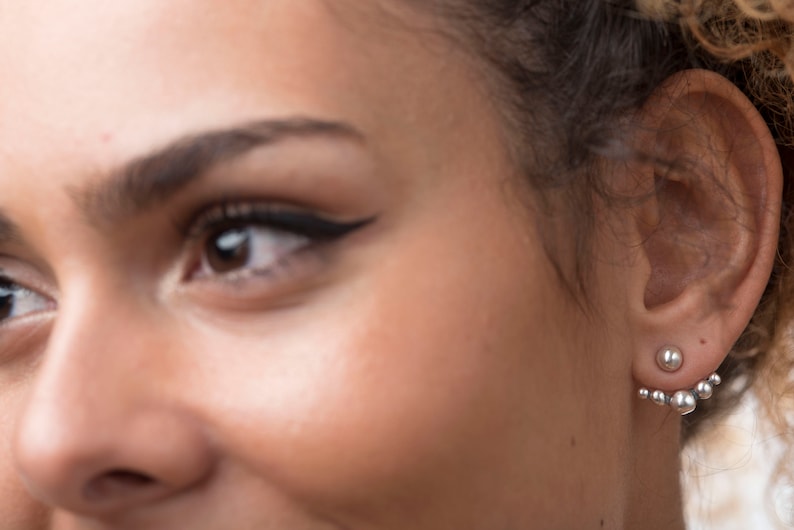 May include: A close-up of a person's ear with a silver ear cuff featuring multiple small round beads. The ear cuff is worn on the upper lobe of the ear.