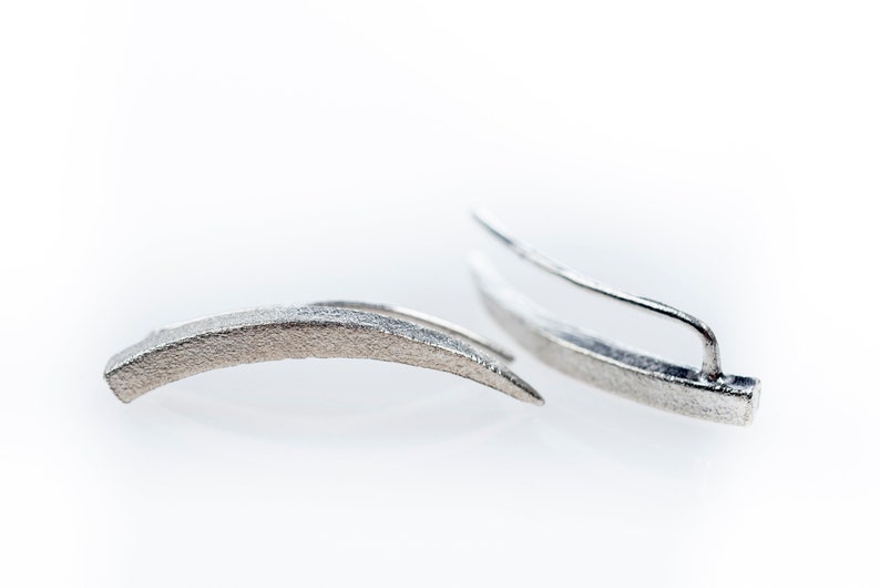 Pu&ograve; includere: Un paio di orecchini d'argento con un design curvo leggermente strutturato. Gli orecchini sono semplici e moderni.