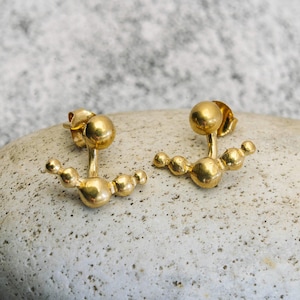 May include: A pair of gold-toned earrings with a curved design featuring multiple small spheres. The earrings are designed to be worn on the upper earlobe.