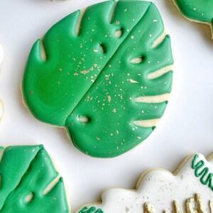 May include: Green sugar cookies decorated with green icing and gold sprinkles, shaped like monstera leaves.