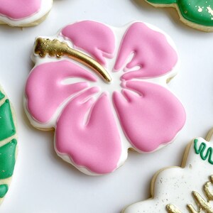May include: Pink and white sugar cookie decorated with a pink hibiscus flower with a gold center. The cookie is on a white background.