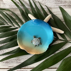 May include: A blue and brown ceramic dish with a scalloped edge. A small, white and green turtle figurine is in the center of the dish.