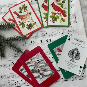 May include: Four playing cards with a Christmas theme. Two cards feature red cardinals on a green background with holly and berries. Two cards feature a red background with a snowy scene and three birds. The cards are from the U.S. Playing Card Co. 1993 Edition.