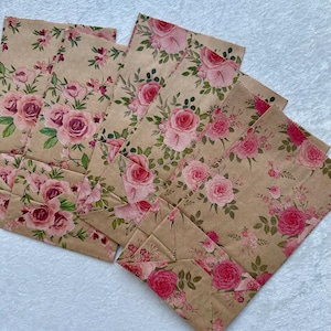 May include: A collection of rectangular paper bags made from light brown kraft paper. Each bag features a repeating floral pattern consisting of various shades of pink roses, small pink blossoms, and green leaves scattered across the surface.
