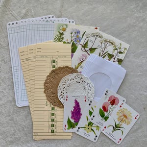 May include: A collection of vintage ephemera, including lined paper, time cards, floral cards, doilies, and playing cards. The playing cards feature botanical illustrations of flowers. The color palette includes beige, white, and brown.