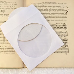 May include: A white paper CD envelope with a round cut-out window, lying on top of a book with musical notation and the text "THE STRING ORCHESTRA".