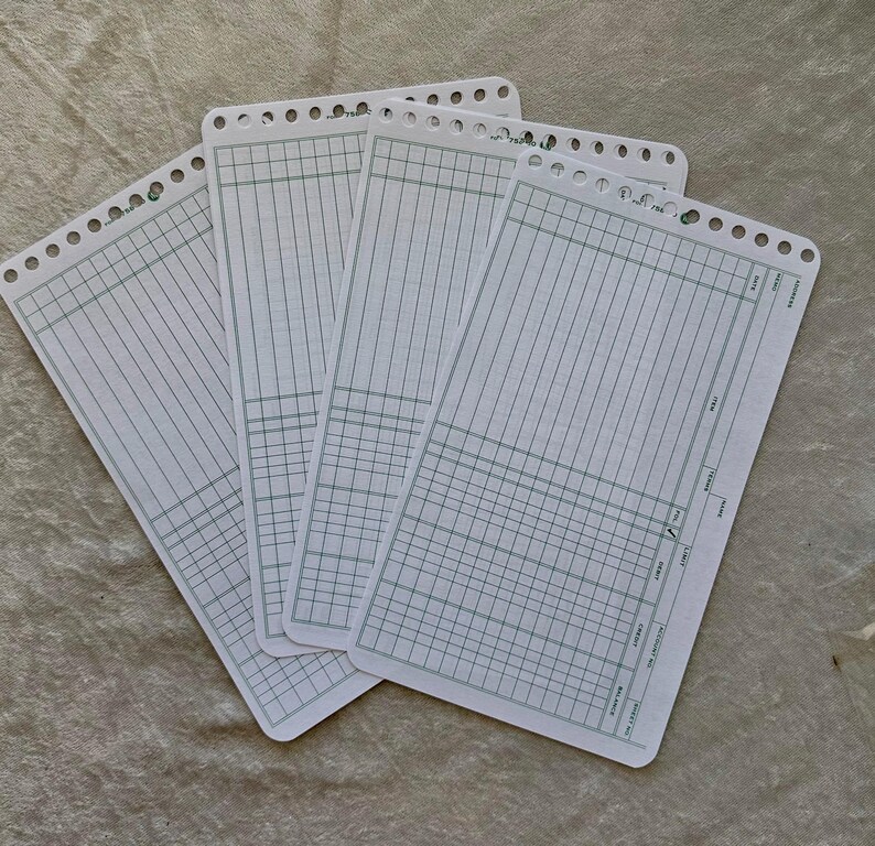 May include: Four white accounting ledger sheets with green grid lines and pre-punched holes along the top edge. The sheets are arranged in a slightly overlapping pattern, displaying columns for item, date, and balance.