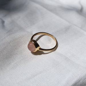 May include: A gold ring with a pink oval gemstone