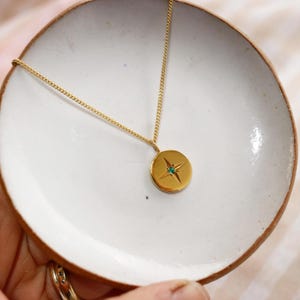 May include: A gold necklace with a round pendant featuring a four-pointed star with a green gemstone in the center.