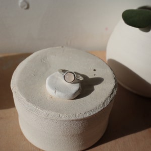 May include: A silver ring with a round, light pink gemstone