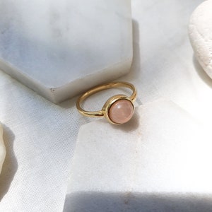 May include: A gold ring with a round, light pink gemstone