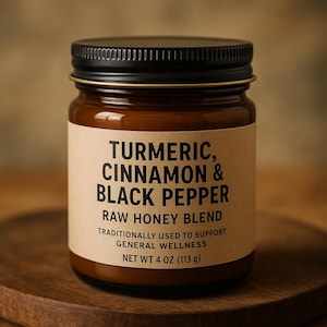 May include: A glass jar of raw honey blend with a black lid and a brown label. The label reads "TURMERIC, CINNAMON & BLACK PEPPER" and "NET WT 113 g". The jar is on a wooden surface.