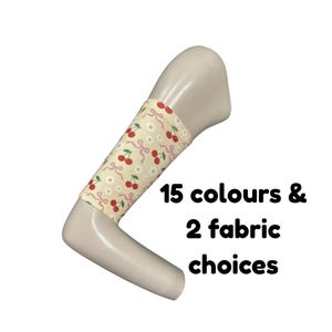 Puede incluir: Una manga de tela de color amarillo claro con un patrón repetitivo de cerezas rojas, margaritas blancas y cintas rosas sobre un brazo de maniquí. El texto 15 colours & 2 fabric choices aparece en negro junto a la manga sobre fondo blanco.