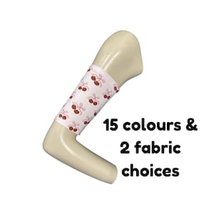 Puede incluir: Una manga de tela rosa claro con un patrón repetitivo de cerezas de color rojo oscuro con tallos y lazos, colocada en un brazo de maniquí beige. El texto 15 colours & 2 fabric choices aparece en negro junto al brazo del maniquí.