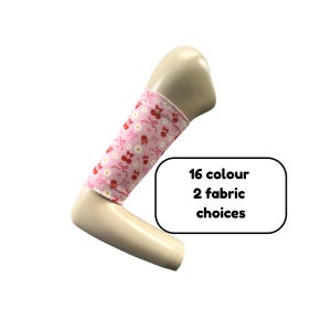 Puede incluir: Una manga para brazo de color rosa claro con un patrón repetitivo de cerezas rojas, margaritas blancas y lazos rosas. La manga se muestra en un brazo de maniquí e incluye un gráfico rectangular blanco con el texto 16 colour 2 fabric choices.