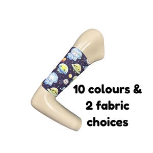 Puede incluir: Una funda de mango en forma de L de color beige con una manga de tela azul oscuro que presenta un patrón repetitivo de astronautas, planetas y platillos voladores de dibujos animados. El texto 10 colours & 2 fabric choices aparece al lado.