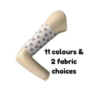 Puede incluir: Un brazo de maniquí beige con una manga de tela blanca que presenta un patrón repetitivo de pequeños koalas grises y estrellas amarillas. El texto 11 colours & 2 fabric choices está impreso en negro junto al brazo sobre un fondo blanco.