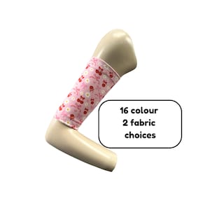 Puede incluir: Una manga para brazo de color rosa claro con un patrón repetitivo de cerezas rojas, margaritas blancas y lazos rosas. La manga se muestra en un brazo de maniquí e incluye un gráfico rectangular blanco con el texto 16 colour 2 fabric choices.