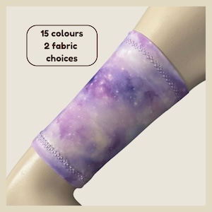 May include: A purple and white galaxy-patterned arm sleeve with a stitched hem. The text 15 colours 2 fabric choices is visible in the upper left corner. The sleeve features a soft, blended nebula design with small white speckles throughout.