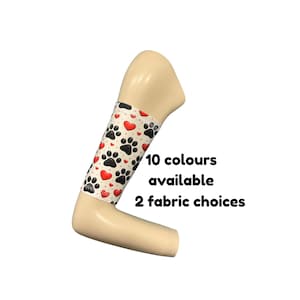 Puede incluir: Un brazo de maniquí beige que lleva una manga blanca con un patrón repetitivo de huellas de patas negras y corazones rojos. El texto a la derecha dice: 10 colours available, 2 fabric choices. La manga cubre el área del antebrazo del maniquí.