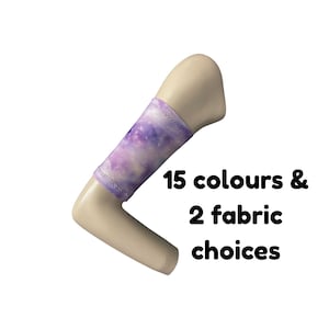 Puede incluir: Un brazo de maniquí beige que lleva una manga de tela con un patrón de galaxia en violeta y blanco. El texto 15 colours & 2 fabric choices está impreso en negro junto al brazo, indicando las opciones disponibles para este accesorio.