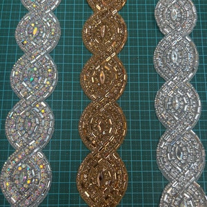 May include: Three rows of beaded trim in silver, gold, and white. The trim is made of small, round beads that are arranged in a repeating pattern. The trim is shown on a green grid background.
