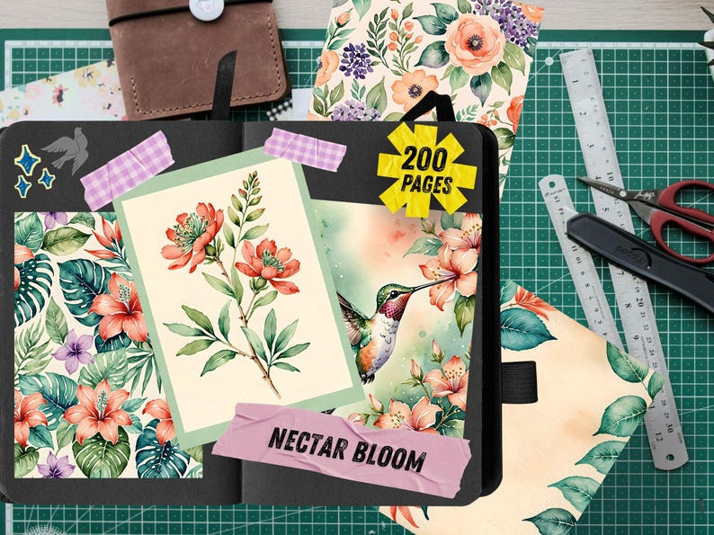 Pu&ograve; includere: Un diario nero con un design floreale, con un colibr&igrave; e la scritta "Nectar Bloom". Il diario include un adesivo che dice "200 pagine". Sono visibili anche altri articoli di cancelleria, tra cui un taccuino in pelle marrone, righelli e forbici.
