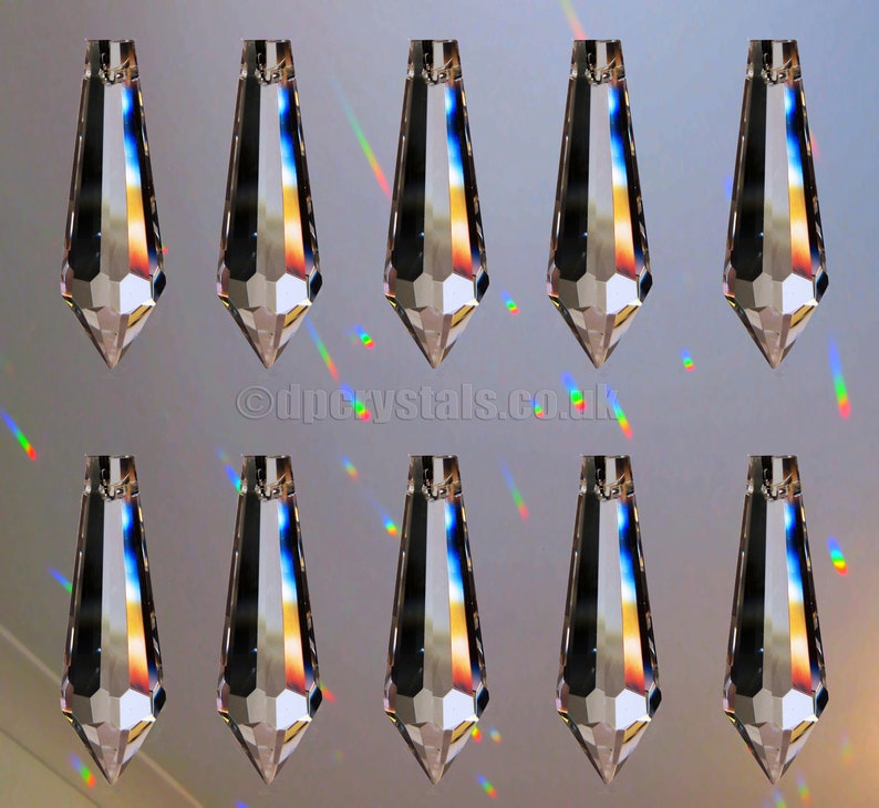 Op de afbeelding: Tien heldere kristallen druppelvormige prisma's met gefacetteerde randen, hangend aan een plafond of ander oppervlak. De prisma's reflecteren regenboogkleuren.