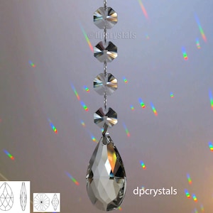 Op de afbeelding: Een kristallen kroonluchterprisma met een traanvorm en een ketting van achthoekige kristallen. Het prisma hangt aan het plafond en werpt regenbogen op de muur. dpcrystals