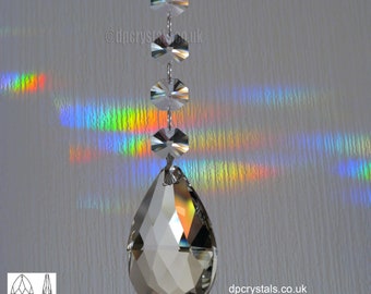 Puede incluir: Un atrapasol de cristal en forma de lágrima con un diseño facetado cuelga de una cadena con cuatro cuentas de cristal más pequeñas. El atrapasol proyecta arcoíris en la pared detrás de él.