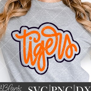 May include: Orange and black "Tigers" text design on a gray t-shirt. The text is in a handwritten style with a thick black outline.