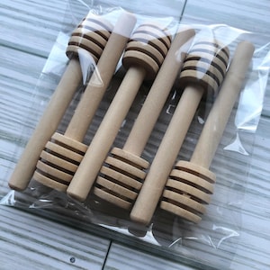 以下が含まれることがあります： 透明なプラスチック袋に入った木製のハチミツディッパー6本。ディッパーは薄い茶色で、らせん状のデザインになっています。